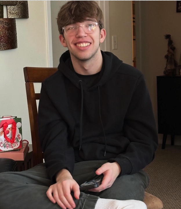 Alex sitting on a couch at home, smiling, at Christmastime