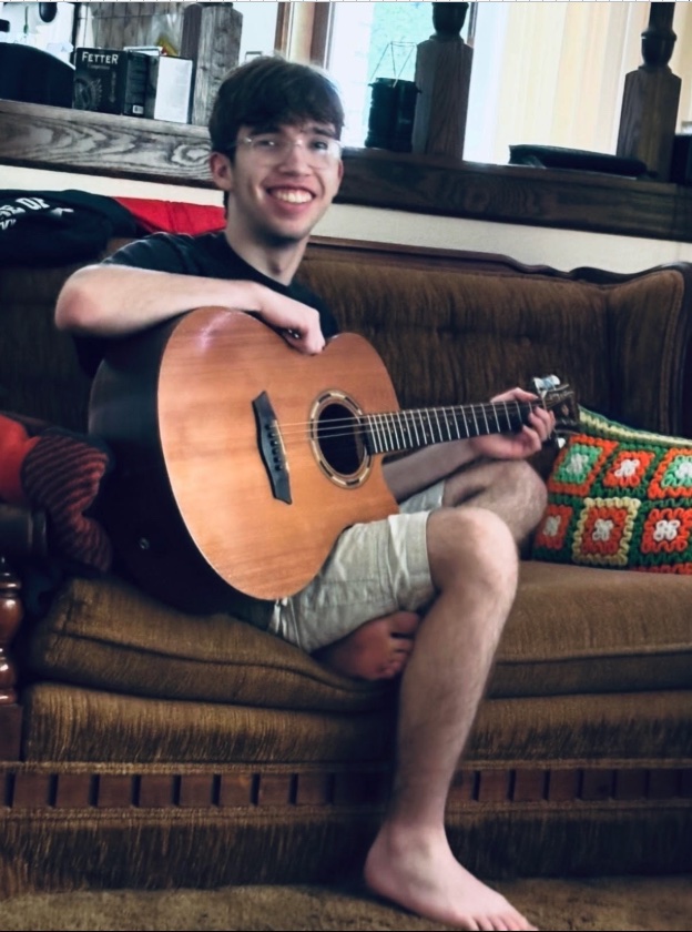 Alex playing an acoustic guitar on the couch at home