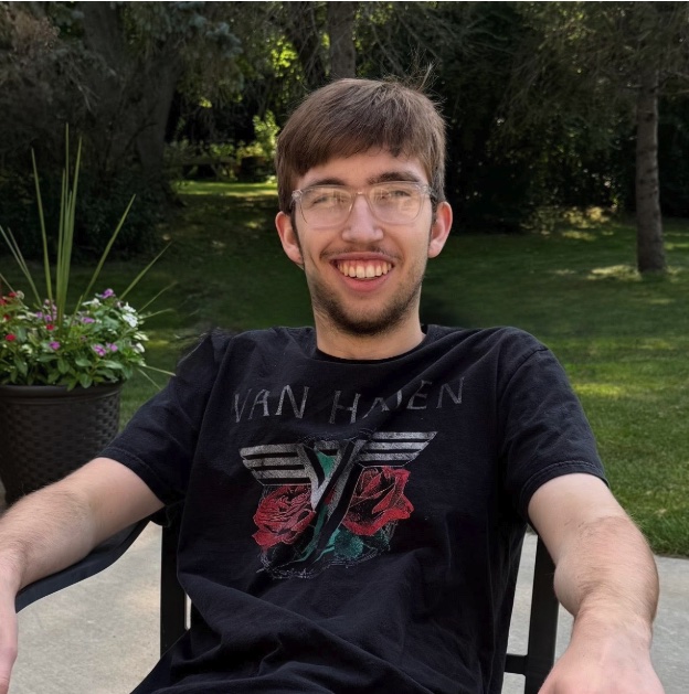 Alex smiling outdoors in a garden, wearing a Van Halen t-shirt