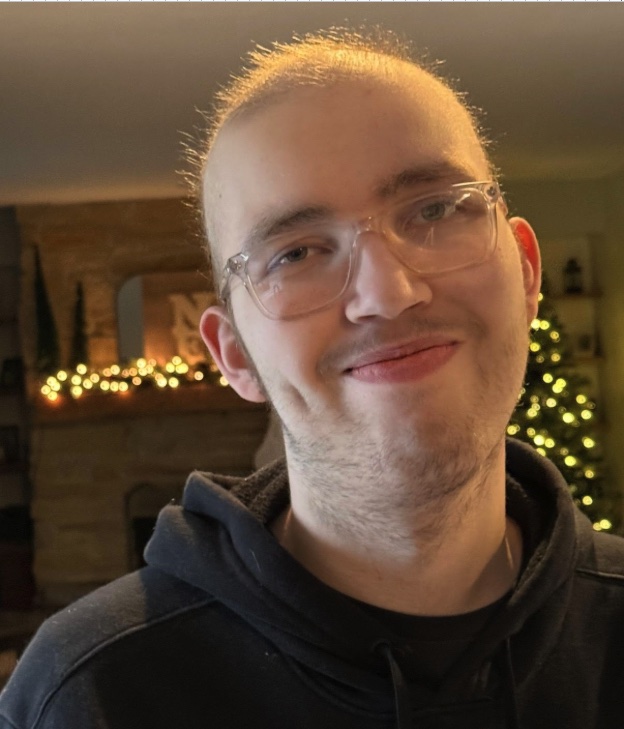A close-up portrait of Alex smiling by a lit Christmas tree